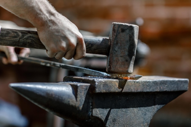 Blacksmith working metal with hammer on the anvil in the forge