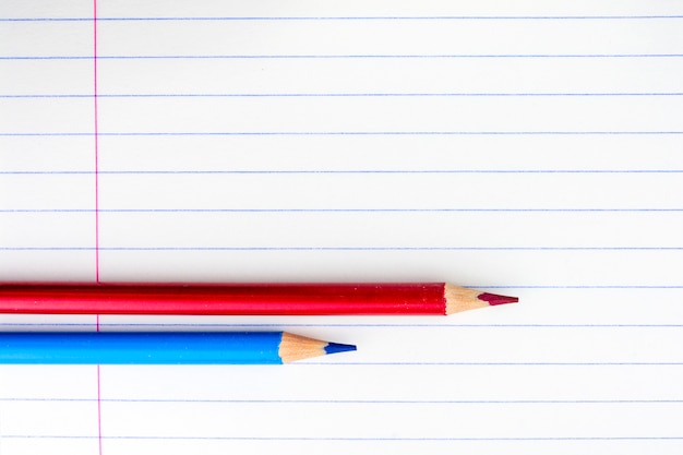 Blad van een schoolnotitieboekje in het gamma. twee potloden op het blad. rode en blauwe potloden.