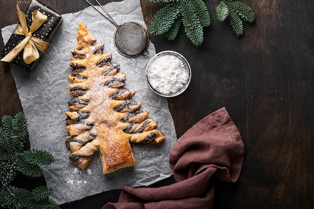 Bladerdeeg kerstboom met chocoladepasta, bestrooid met poedersuiker op oude donkere houten achtergrond. Kerst of kerst gebak. Bovenaanzicht. Ruimte kopiëren