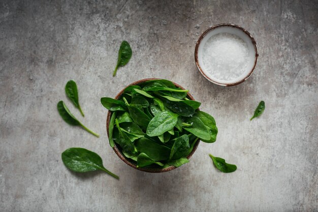 Bladeren van verse babyspinazie in een Kom. Bovenaanzicht van donkere biologische groene bladeren en zout. Gezond veganistisch voedsel lifestyle concept. Bovenaanzicht