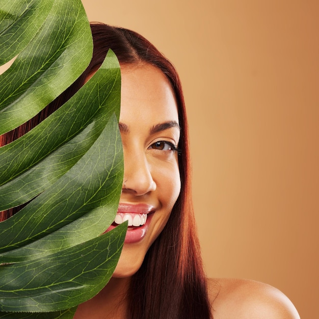 Bladschoonheid en portret van een gelukkige vrouw in studio voor natuurlijke dermatologiecosmetica of wellness Huidverzorging natuur en monsteraplant voor milieuvriendelijke gezichtsbehandeling van modelpersoon op bruine achtergrond