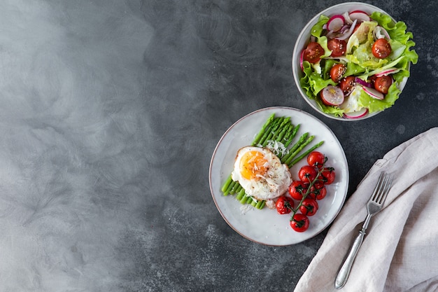 Blanched asparagus, fried egg, tomatoes and sald on the bowl, top view.