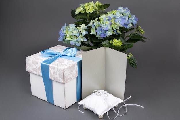 Blanco cadeaubon boeket van hortensia bloemen geschenkdoos en trouwringen over grijze achtergrond