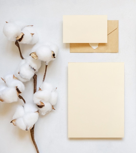 Blanco kaarten en envelop met katoenen bloemen bovenaanzicht op witte bruiloft mockup