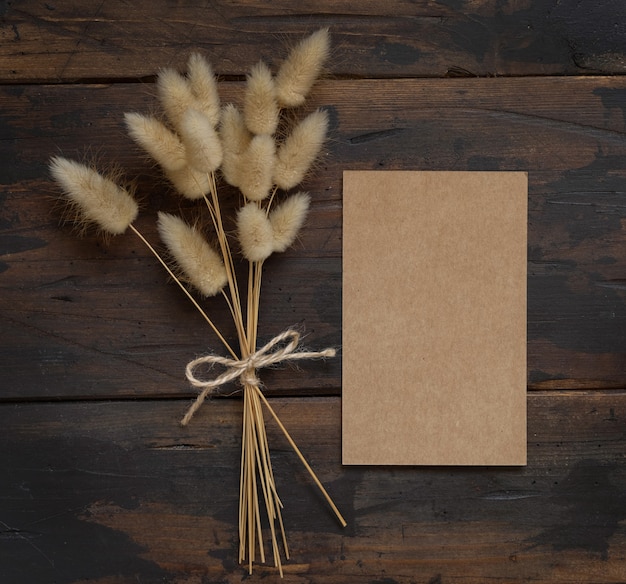 Foto blanco kraftpapier kaart op bruin houten tafel met gedroogde bloemen boeket opzij bovenaanzicht