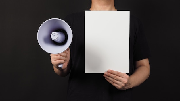 Foto blanco leeg papier in iemands hand met megafoon op zwarte achtergrond.