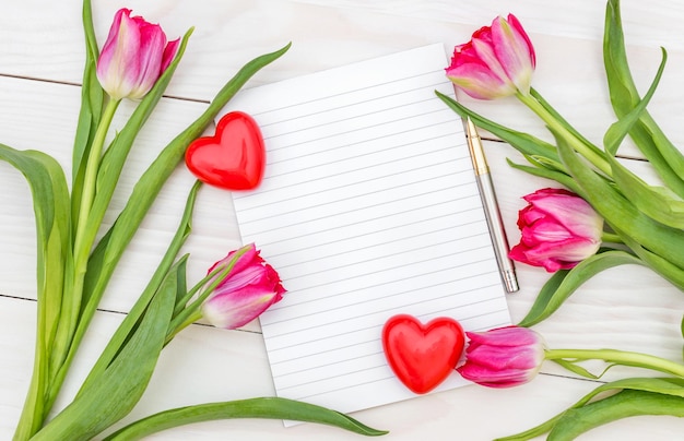 Blanco notitieblok met twee harten en boeket met tulpen op de witte houten tafel bovenaanzicht