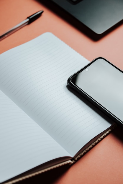 Blanco notitieblok staat bovenop een kleurenbureautafel met laptopcomputer, telefoon en benodigdheden. Bovenaanzicht met kopieerruimte, plat gelegd. Minimaal concept, werkruimte