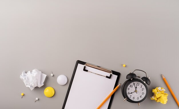 Blanco papier op klembord witte wekker en briefpapier bovenaanzicht op grijze achtergrond