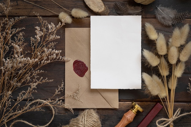 Blanco papieren kaart op verzegelde envelop en houten tafel met gedroogde planten bovenaanzicht Boho mockup scene met