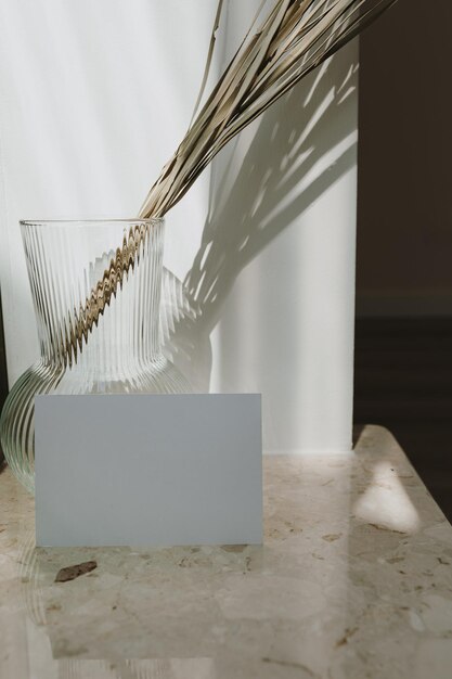 Blanco papieren kaartblad met lege kopie ruimte Gedroogd palmblad in stijlvolle vaas op marmeren tafel Schaduwen op de muur Silhouet in zonlicht Branding zakelijke uitnodigingskaart met copyspace