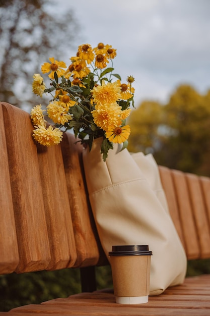 Blanco papieren kopje afhaalkoffie met bloemboeket in zak op bankje in herfstpark