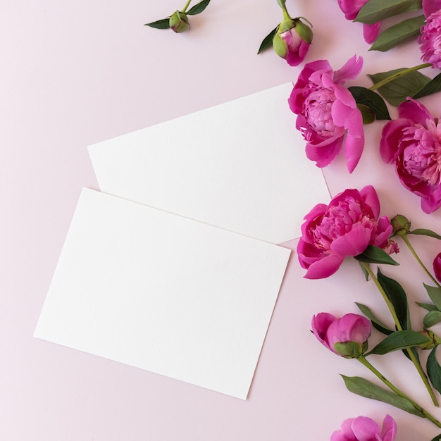 Blanco papieren uitnodigingskaarten Roze pioen bloemen boeket op neutrale pastel elegante roze achtergrond Plat lag bovenaanzicht minimale bloemensamenstelling