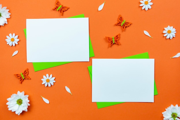 Blanco wenskaarten mockup op kleurrijk oranje oppervlak met margriet bloemen en vlinders decoratie