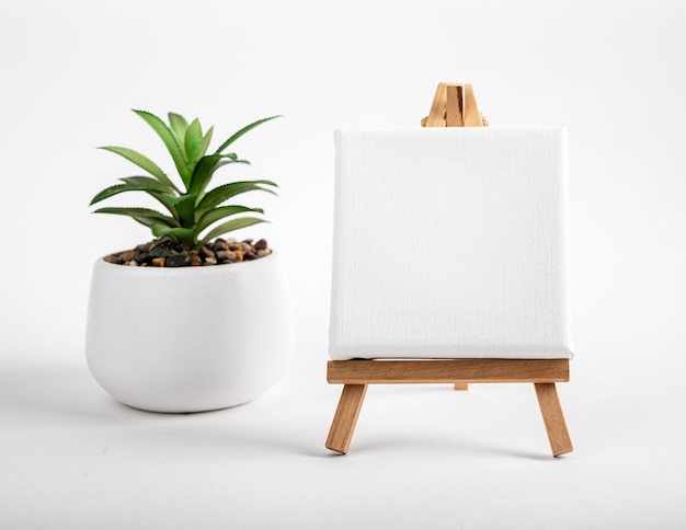 Blanco wit canvas mock up leeg papier op mini houten statief schildersezel en ingemaakte kamerplant op bureau