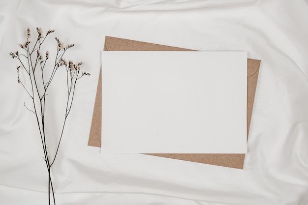 Blanco wit papier op bruine papieren envelop met droge bloem van Limonium op witte doek