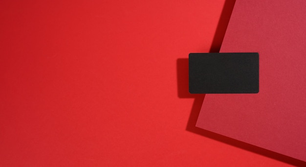 Foto blanco zwart rechthoekig visitekaartje ligt op een modern rood oppervlak met rode vellen papier met een schaduw. zakelijke sjabloon, plat, banner