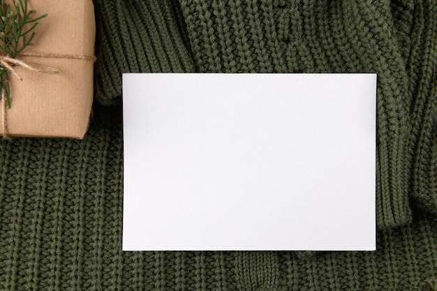 니트 녹색 스웨터에 전나무 장식이 있는 빈 7x5 카드 모형 크래프트 선물 상자, 결혼식 초대 디자인 요소, 감사 또는 인사말 카드. 크리스마스 겨울 카드 조롱 배경