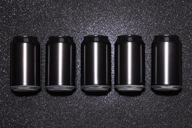 Photo blank black aluminum cans in a row on a black background with sparkles in hard light