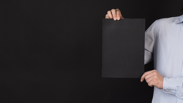 Фото Пустая черная доска на бумаге a4 в человеке, покрытом рукой лицом и одетой в синюю рубашку на черном фоне x9