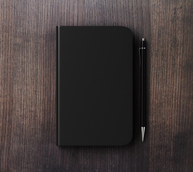 Photo blank black diary cover with pen on brown wooden table mock up