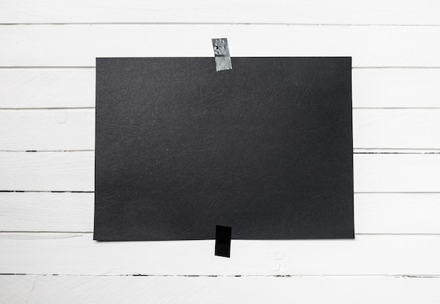 Blank black poster hanging on a tape on white wooden plank wall. Template background for your design.