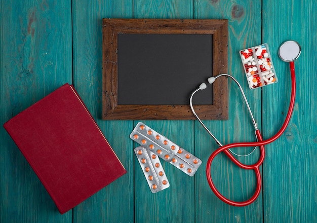 Blank blackboard pills book and stethoscope on wooden background