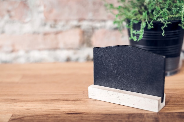 Blank blackboard on wood table top at blur brick background in restaurant