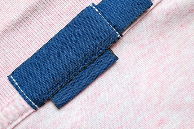 Etichetta di abbigliamento per la lavanderia blu vuoto su sfondo di tessuto di camicia rosa