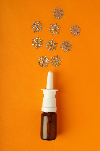 Blank bottle of nasal spray and decorative snowflakes on orange background