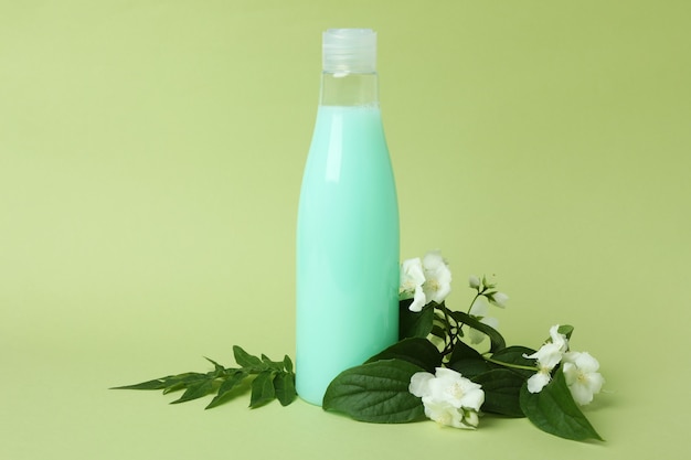 Blank bottle of shampoo and flowers on green