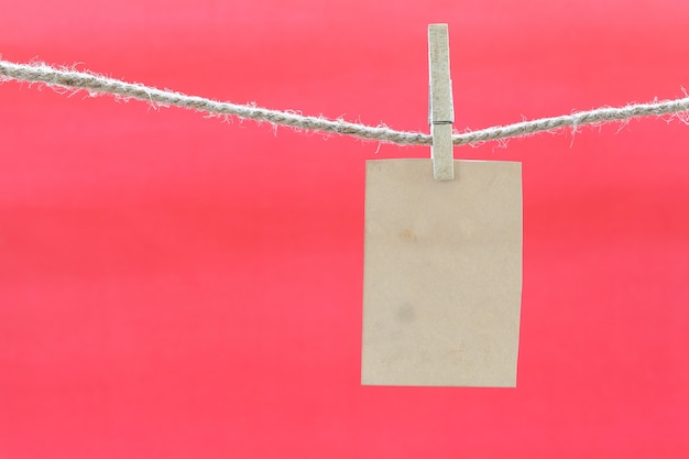 Photo blank brown note on clothesline and red background.