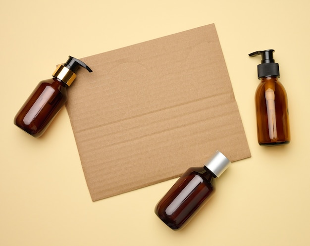 Blank brown sheet of corrugated paper and brown glass bottles with dispenser beige background. Packaging for gel, serum, advertising and promotion. Natural organic products. Mock up