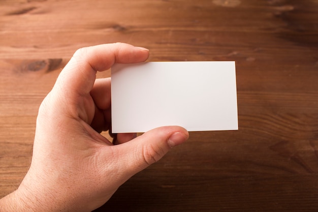 Blank business card in a hand on a wooden background