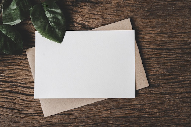 A blank card is placed on envelope and leaf with wood background