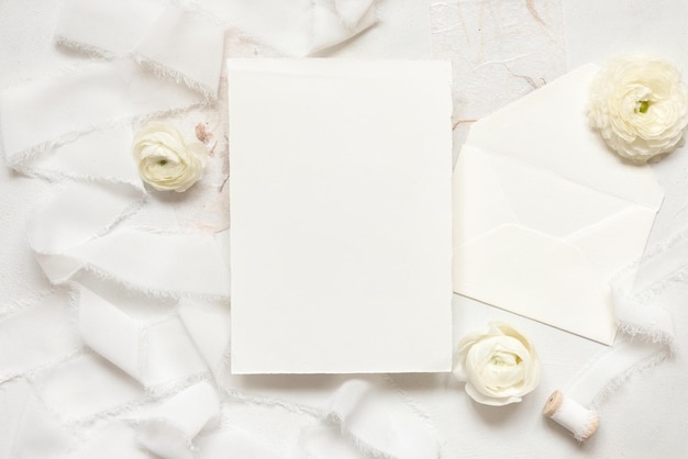 Blank card near cream roses and white silk ribbons top view wedding mockup