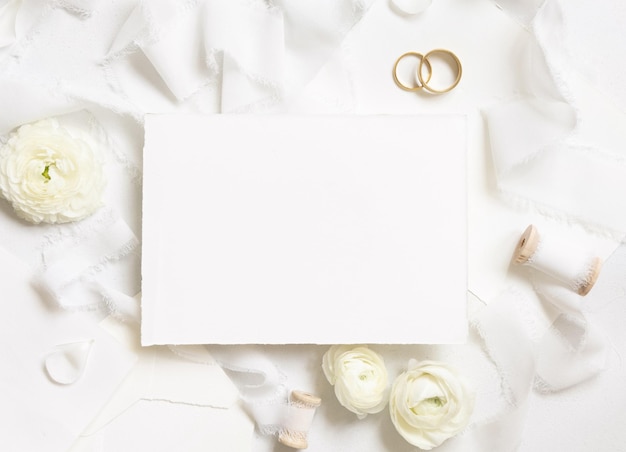 Blank card near cream roses white silk ribbons and wedding rings top view wedding mockup