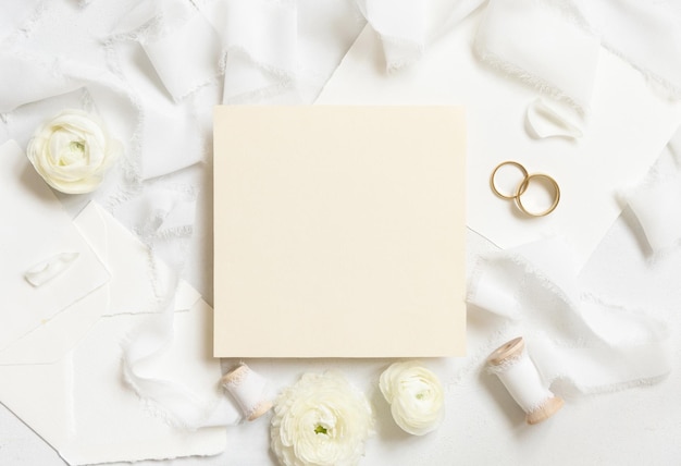 Foto carta bianca vicino a rose crema nastri di seta bianca e fedi nuziali vista dall'alto matrimonio mockup