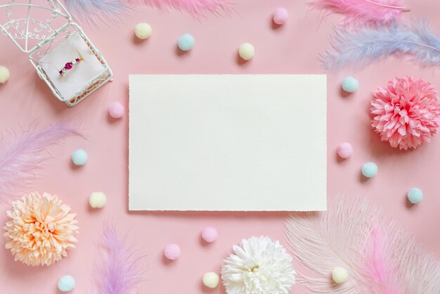 Photo blank card between pastel flowers pompoms and feathers near ring in a gift box on pink top view