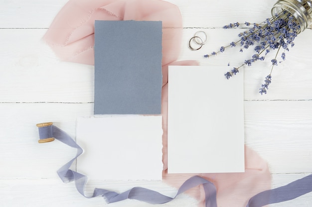 Blank card and ribbon with two wedding rings on a background of pink fabric with lavender flowers