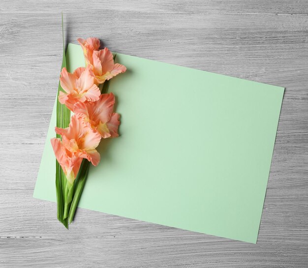 Blank card with beautiful gladiolus on wooden background