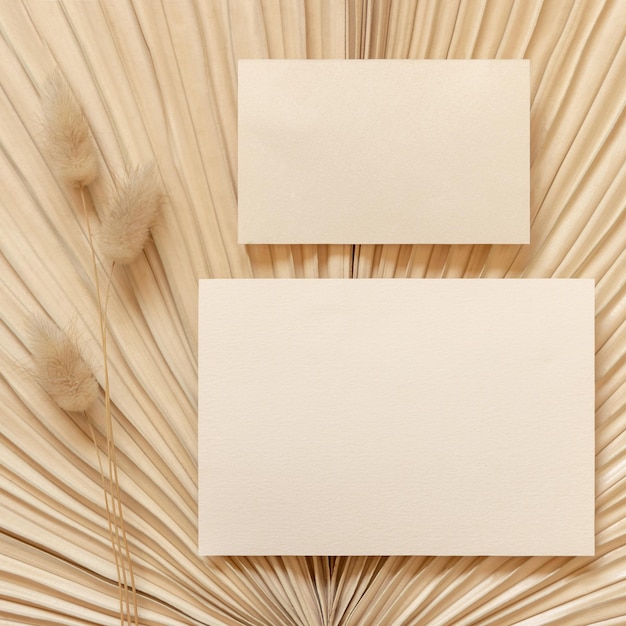 Blank cards on dry beige palm leaf near hare's tail grass top view boho wedding mockup