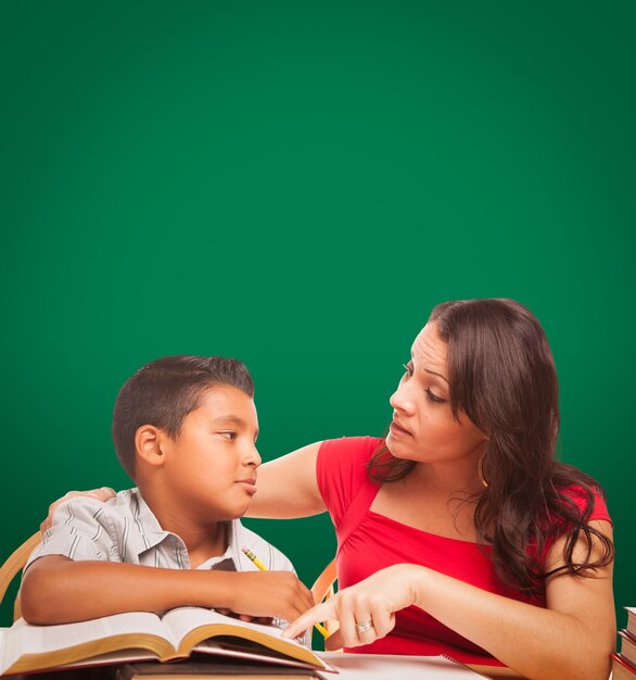 Photo blank chalk board behind hispanic young boy and famale adult studying