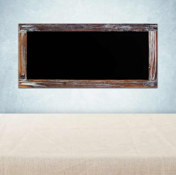 फोटो blank chalkboard hanging on green wall over empty table with sack tablecloth background