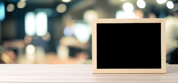 Blank chalkboard standing on wood table over blur restaurant with bokeh background