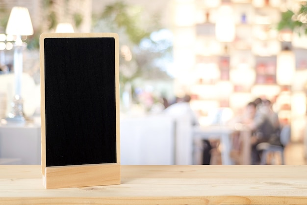 Foto lavagna in bianco che sta sulla tavola di legno sopra il ristorante della sfuocatura con il fondo del bokeh