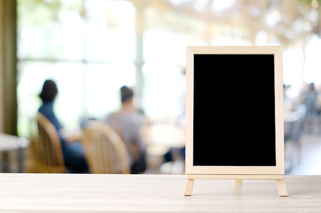 Blank chalkboard standing on wood table over blur restaurant