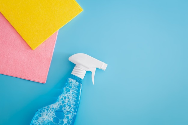 blank cleaning spray bottle and colored rags on blue background flat lay