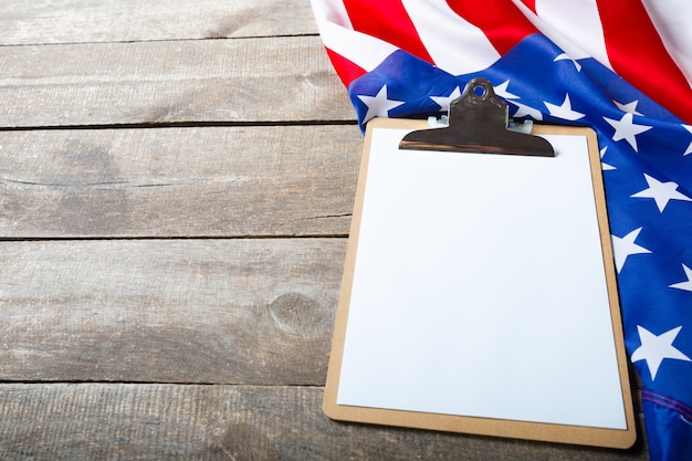 Blank clip board and USA flag on wooden background