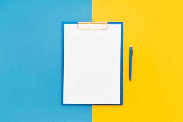 Blank clipboard mockup and blue ballpoint pen on blue-yellow color background